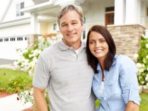 A mature couple standing proudly in front of their home